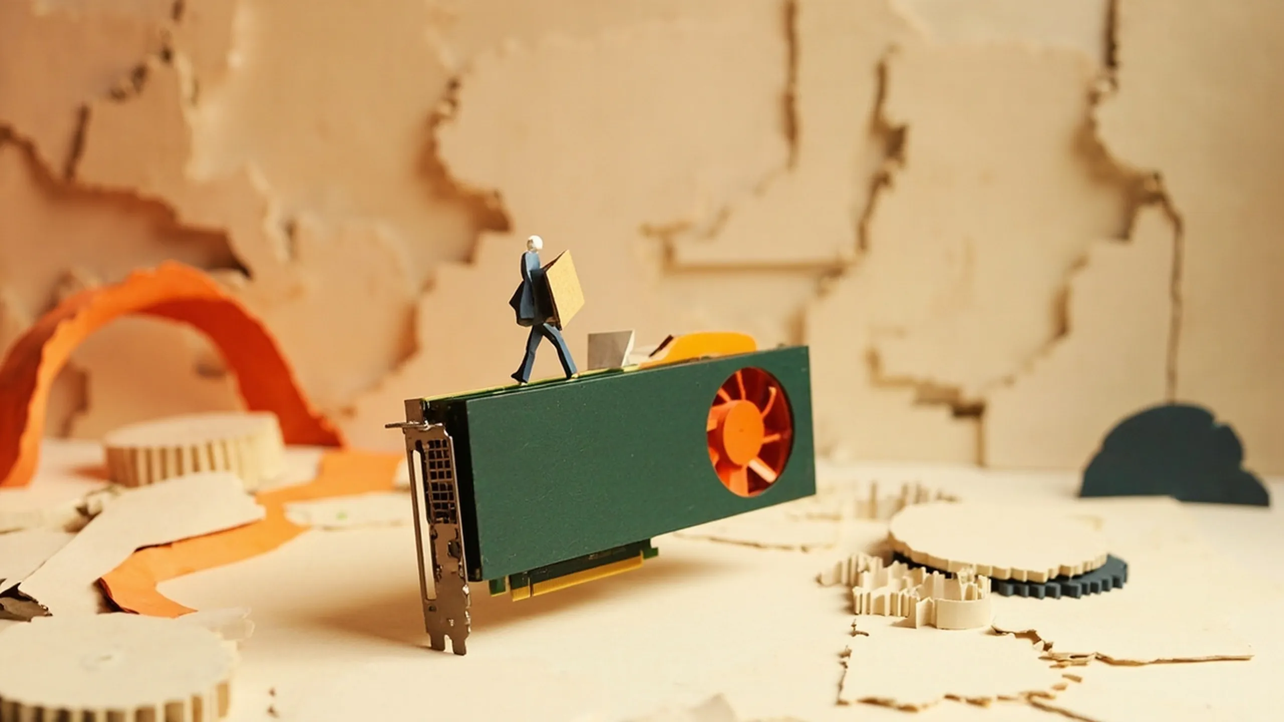 Paper-cutout illustration of a small figure carrying folders and a toolbox across an upright graphics card used as a stage